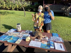 Two people in a garden with a table full of turtle posters